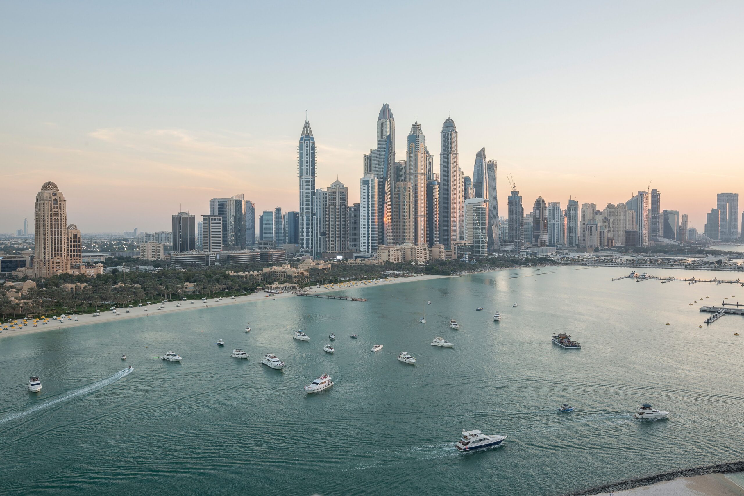Panoramic view of Dubai Marina skyline with boats on the water at dusk.
